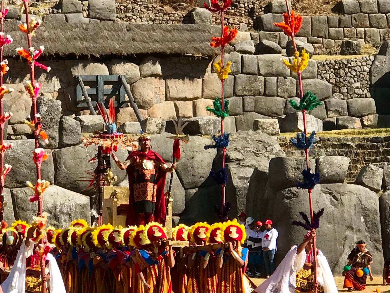 The Sapa Inca arrives to Inti Raymi, Cusco, Peru carried on a long litter carried by a procession of men in bright red costume and bright yellow headgear