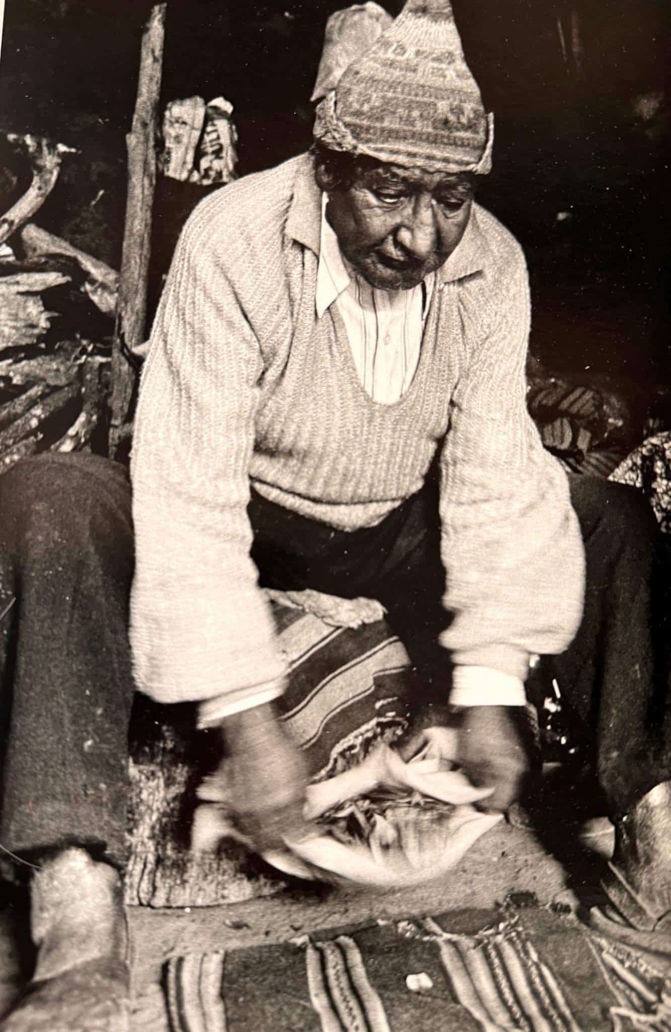 A sepia-toned portrait of Peruvian Maestro don Benito Corihuaman Vargas performing a divination with a bag full of coca leaves.